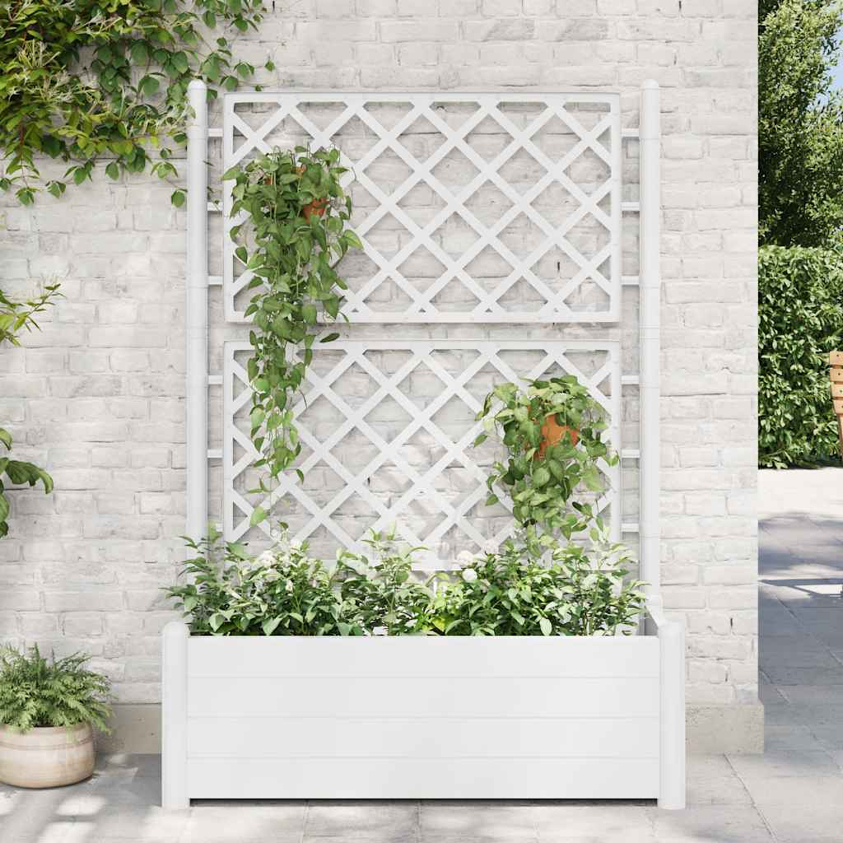 Weißes Spalier mit Pflanzen und Blumen vor einer weißen Backsteinmauer. Eine weiße Pflanzkasten enthält mehr Pflanzen.