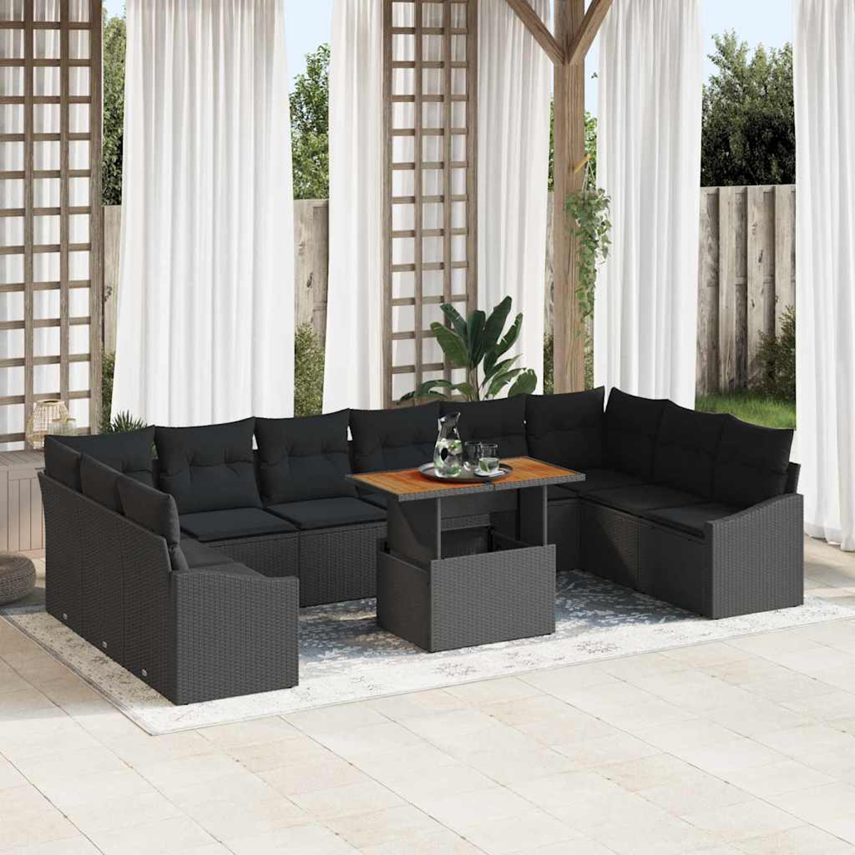 Ein dunkelgraues Outdoor-Ecksofa mit schwarzen Kissen umgibt einen Tisch mit Getränken. Weiße Vorhänge und eine Holzkonstruktion dahinter.