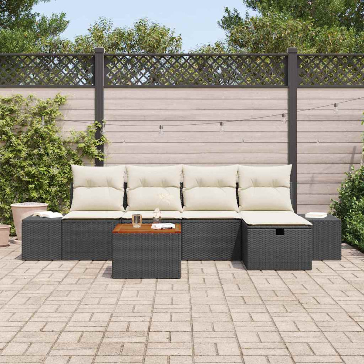 Conjunto de patio al aire libre con muebles de mimbre grises, cojines beige y una pequeña mesa de madera en un patio de ladrillo. Plantas verdes y una valla al fondo.