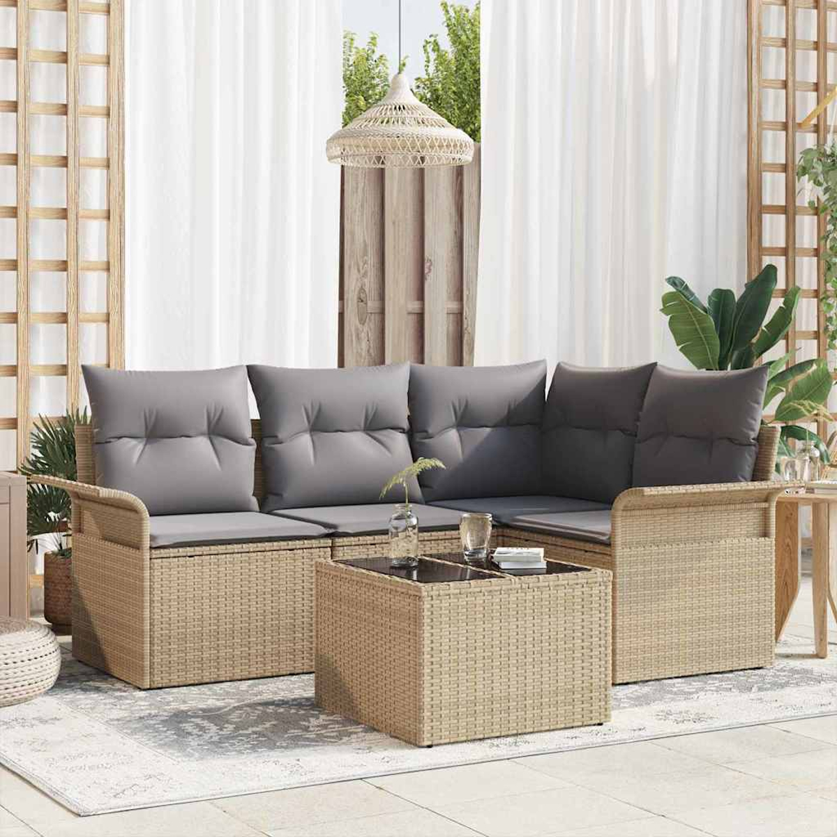 Outdoor-Korbsessel mit grauen Kissen und einem passenden Couchtisch auf einem gemusterten Teppich, in der Nähe eines Fensters mit weißen Vorhängen.