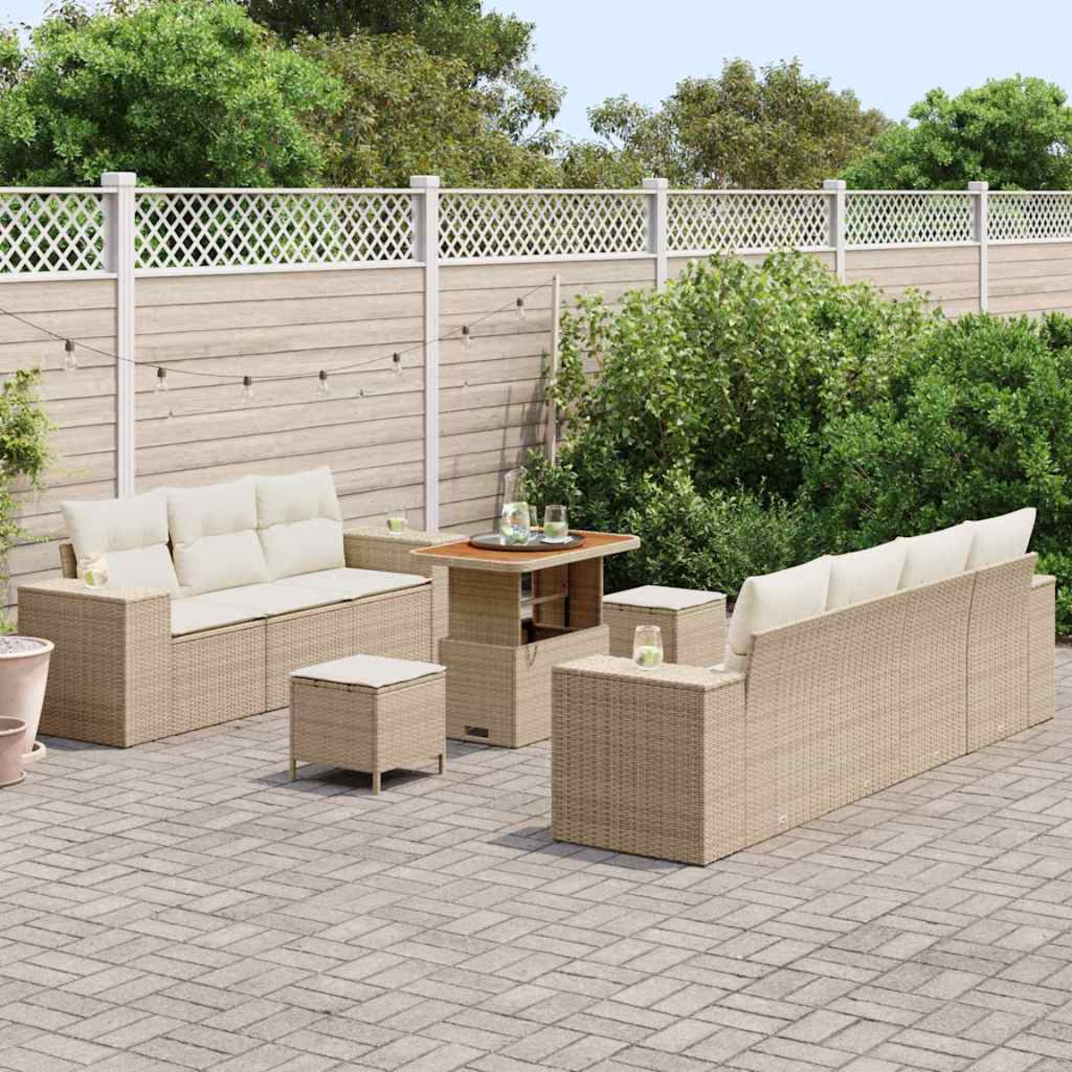 Gartenmöbel-Set aus Korbgeflecht auf einer Terrasse. Beinhaltet ein Sofa, zwei Ottomanen, einen Tisch und ein langes Sofa, alles in neutralen Tönen.