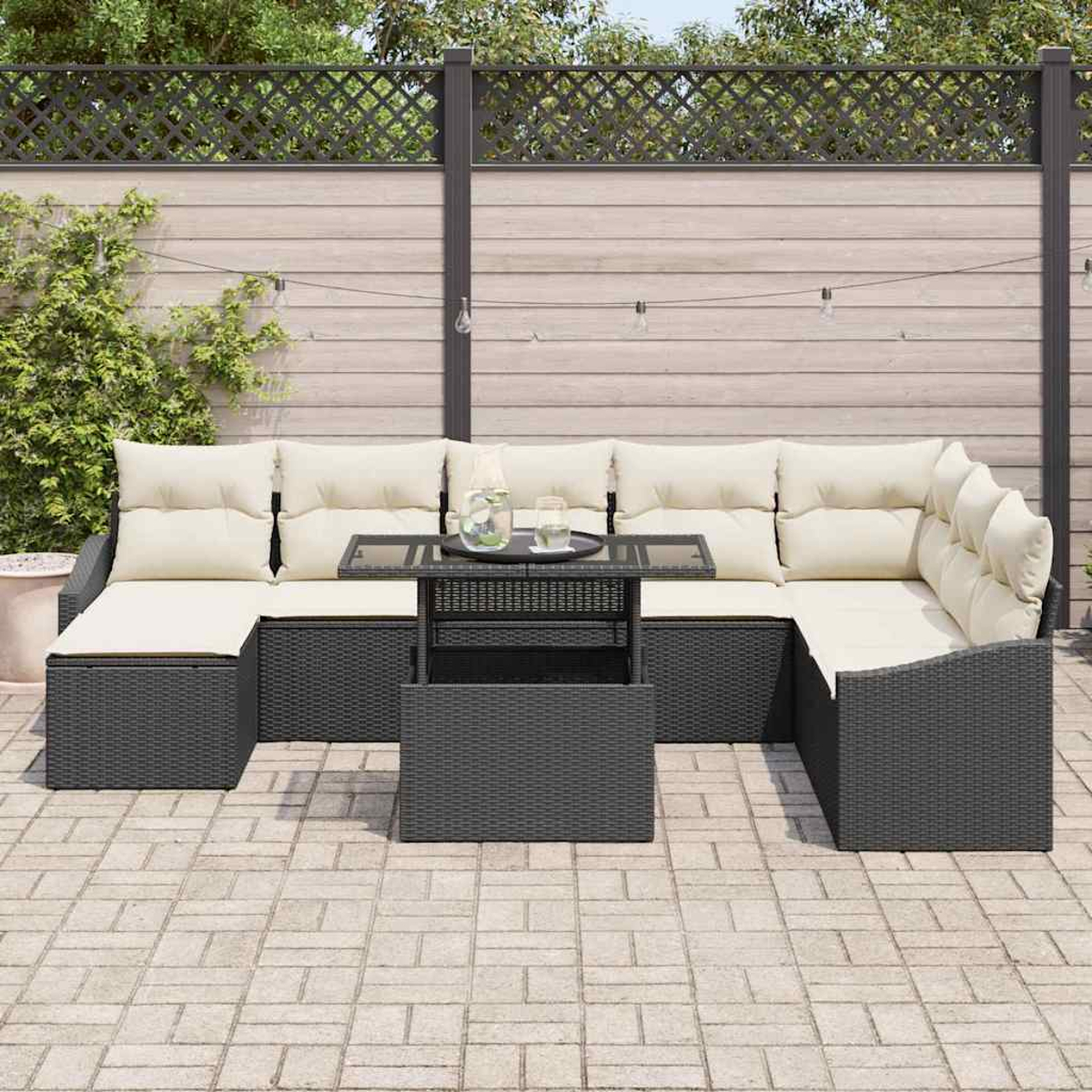 Outdoor-Ecksofa mit cremefarbenen Kissen und einem kleinen Tisch. Es steht auf einer Ziegelterrasse, mit einem Zaun und Grün im Hintergrund.