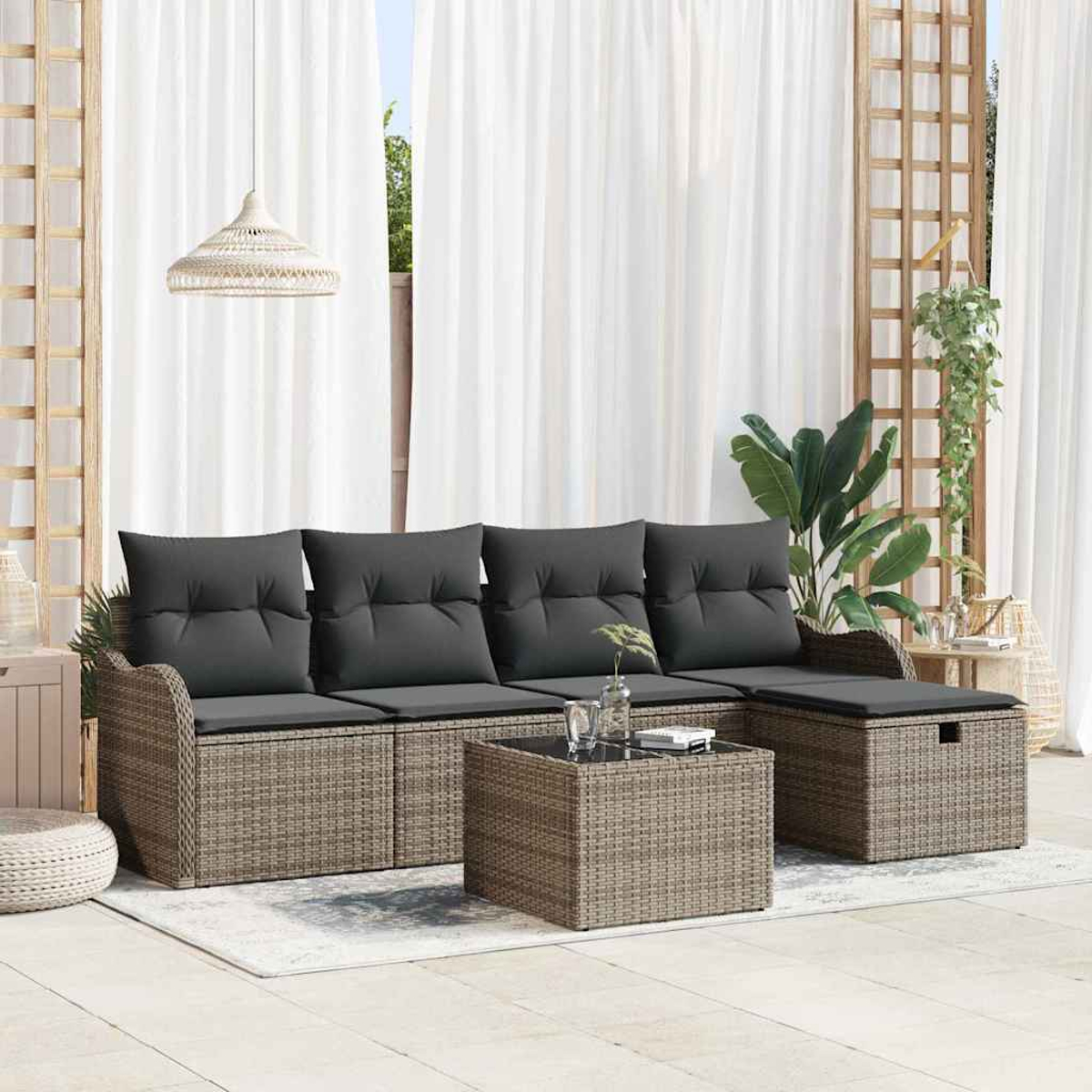 Outdoor-Wicker-Sofa mit grauen Kissen, Couchtisch und Ottoman. Weiße Vorhänge und Pflanzen im Hintergrund, die einen entspannenden Raum schaffen.