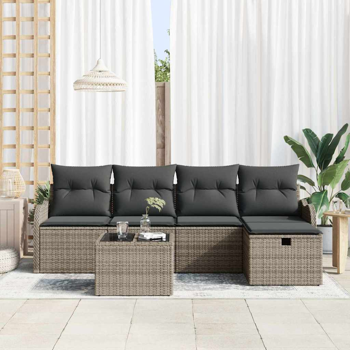 Außenbereich mit grau gepolstertem Sofa, Korbtisch und Pflanzen. Weiße Vorhänge im Hintergrund.