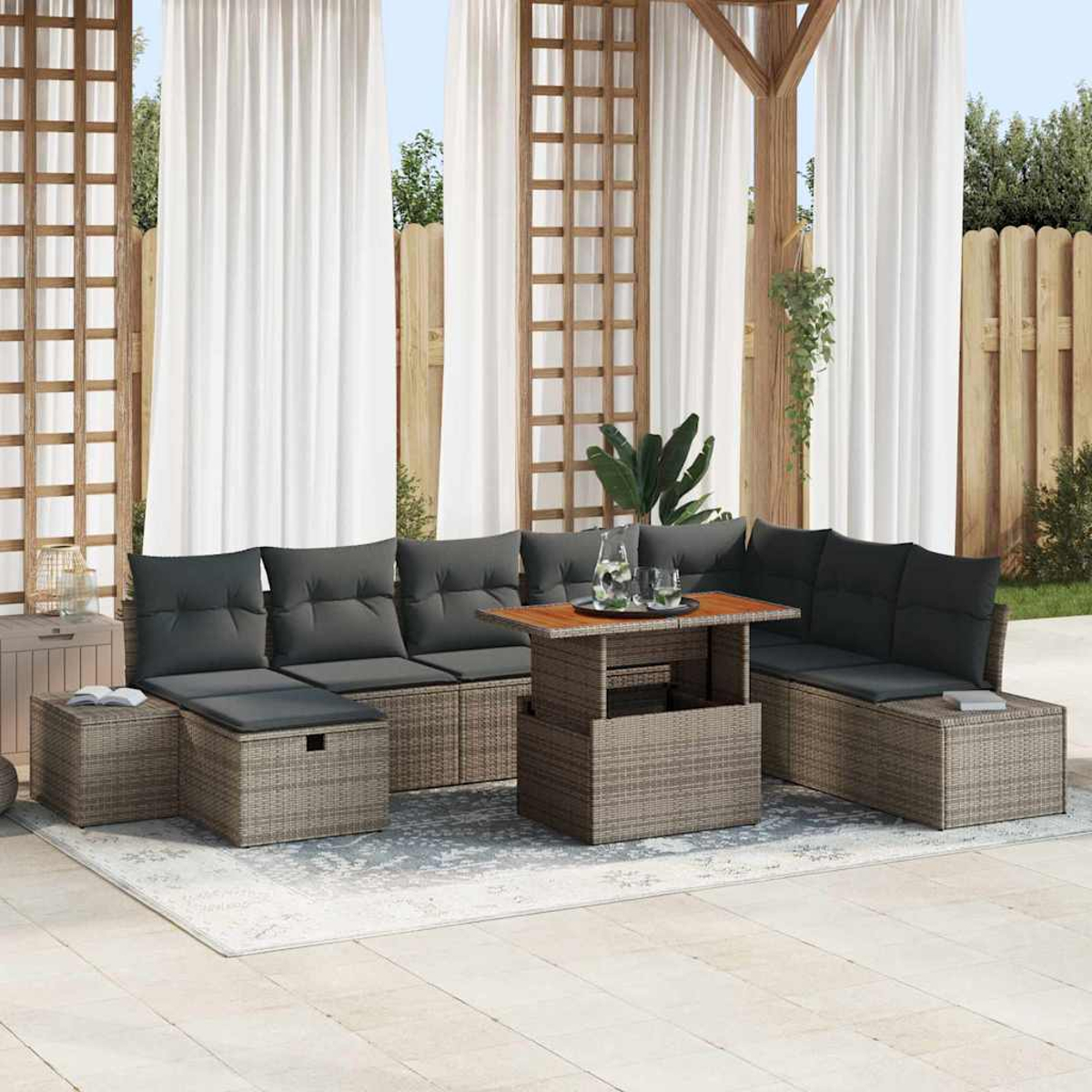 Außenbereich mit grauen Kissen, Korbmöbeln, Holztisch, weißen Vorhängen und Holzzaun im Hintergrund.