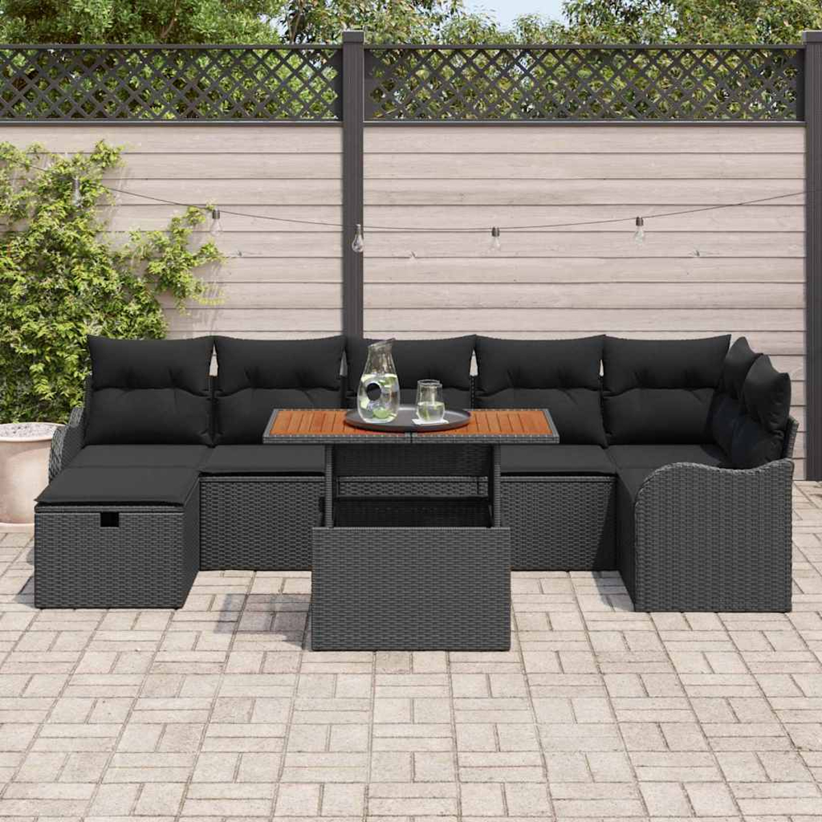 Outdoor-Ecksofa mit schwarzen Kissen und einem Holztisch. Auf einer Steinterrasse mit Zaun und Grün im Hintergrund.