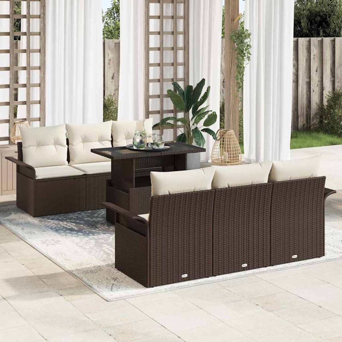Terrassenset mit braunen Korbmöbeln, cremefarbenen Kissen und einem Tisch. Weiße Vorhänge und grüne Pflanzen im Hintergrund.