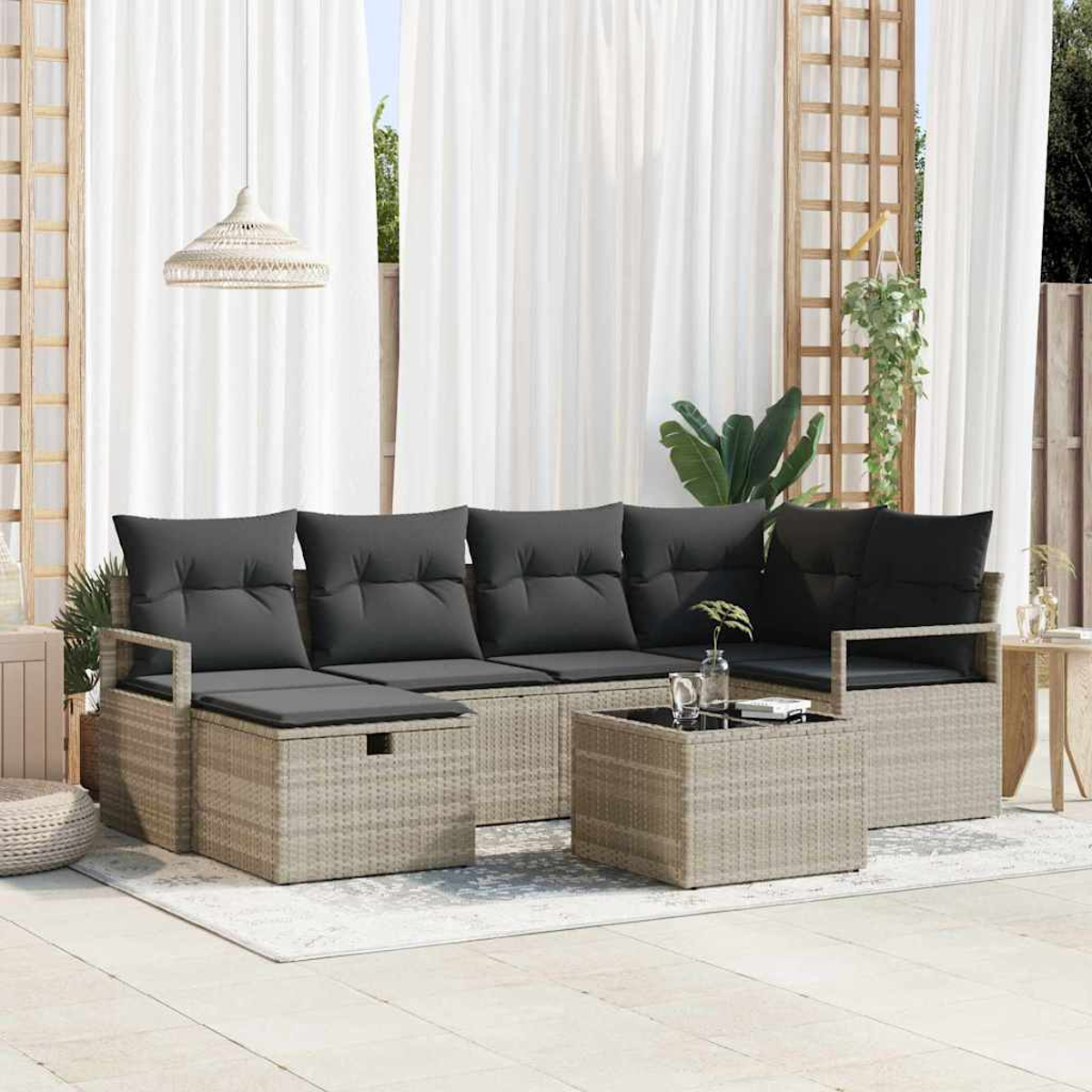 Gartenmöbel-Set mit grauen Kissen, einem Korbtisch und weißen Vorhängen im Hintergrund.