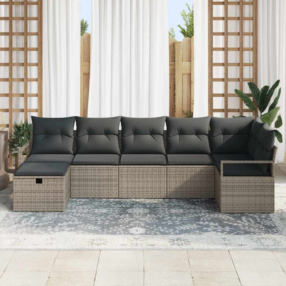Outdoor-Ecksofa mit grauen Kissen. Beiger gewebter Rahmen. Weiße Vorhänge und Holzgitter im Hintergrund. Blau gemusterter Teppich.