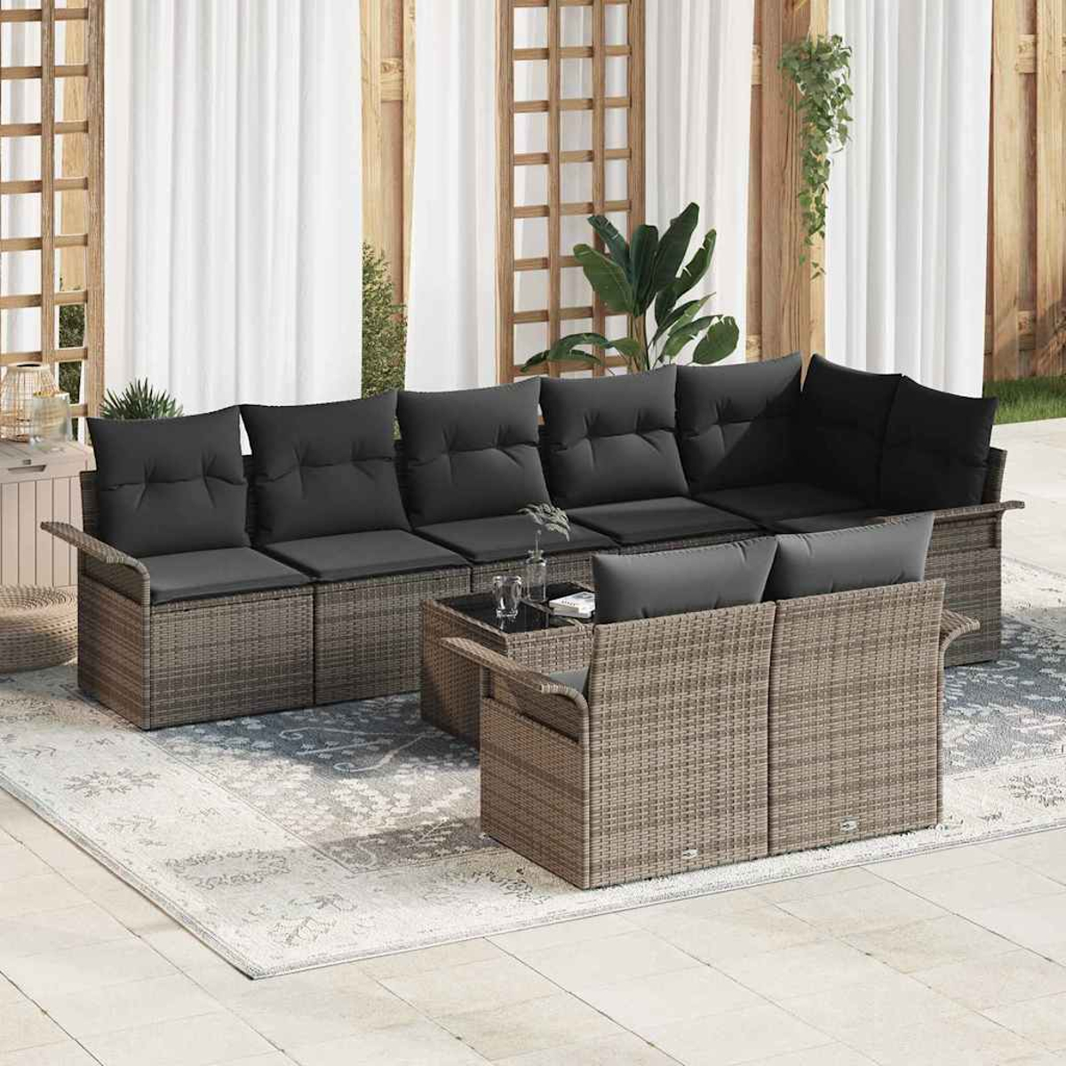 Outdoor-Rattansofa-Set mit schwarzen Kissen, Couchtisch und Teppich. Der Hintergrund hat Vorhänge und Holzgitter.