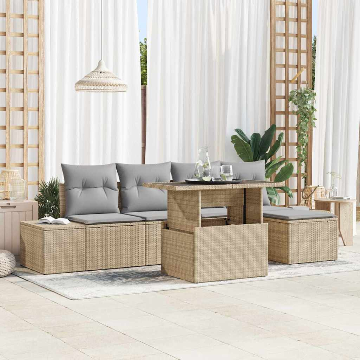 Garten-Sitzgruppe mit Sofa, Tisch und Ottomane. Beige Korbmöbel mit grauen Kissen auf einem weißen Teppich, vor weißen Vorhängen.