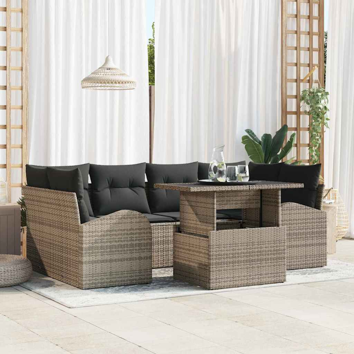 Gartenmöbel-Set aus Korbgeflecht mit Tisch, Sofa und Stühlen. Schwarze Kissen und weißer Vorhang im Hintergrund. Eine Lampe hängt oben.