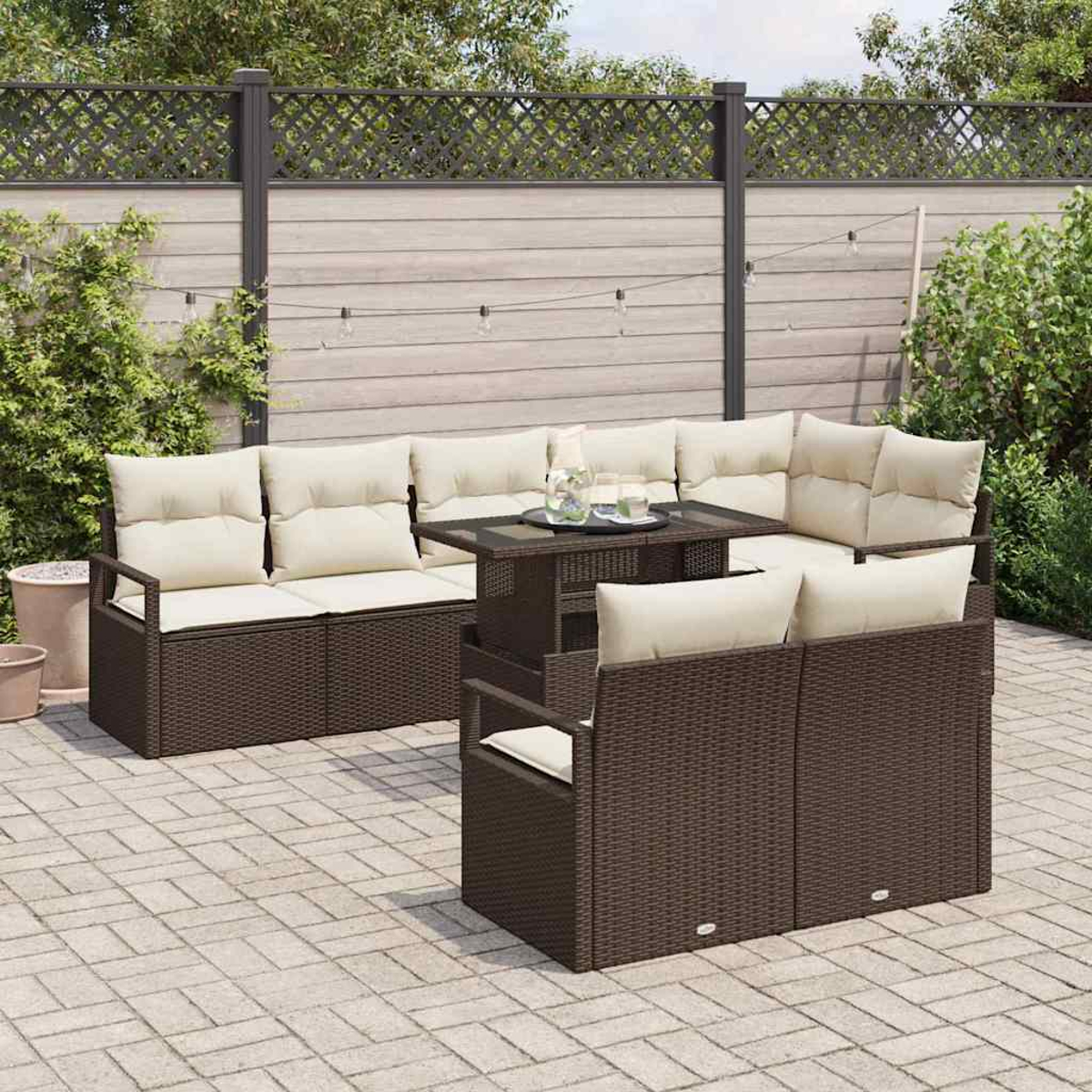 Braunes Outdoor-Korbmöbel-Set mit cremefarbenen Kissen auf einer Ziegelterrasse. Ein Tisch mit Getränken steht in der Mitte, im Hintergrund ein Zaun.