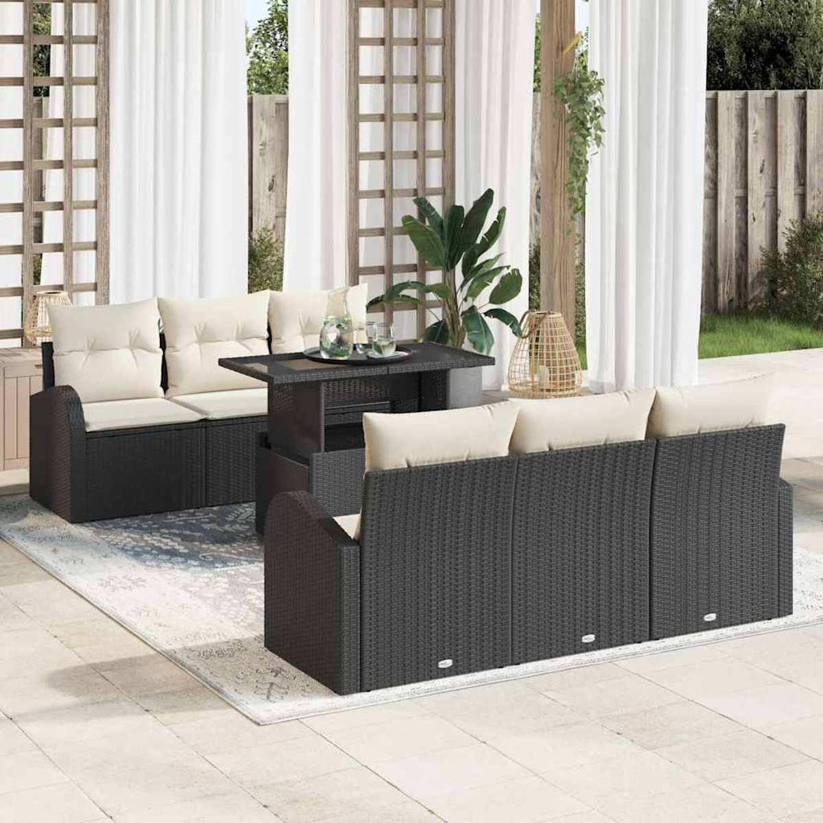 Terrassenmöbel-Set mit schwarzem Korbmöbel, cremefarbenen Kissen, einem Tisch und einem Teppich. Weiße Vorhänge und Pflanzen im Hintergrund.