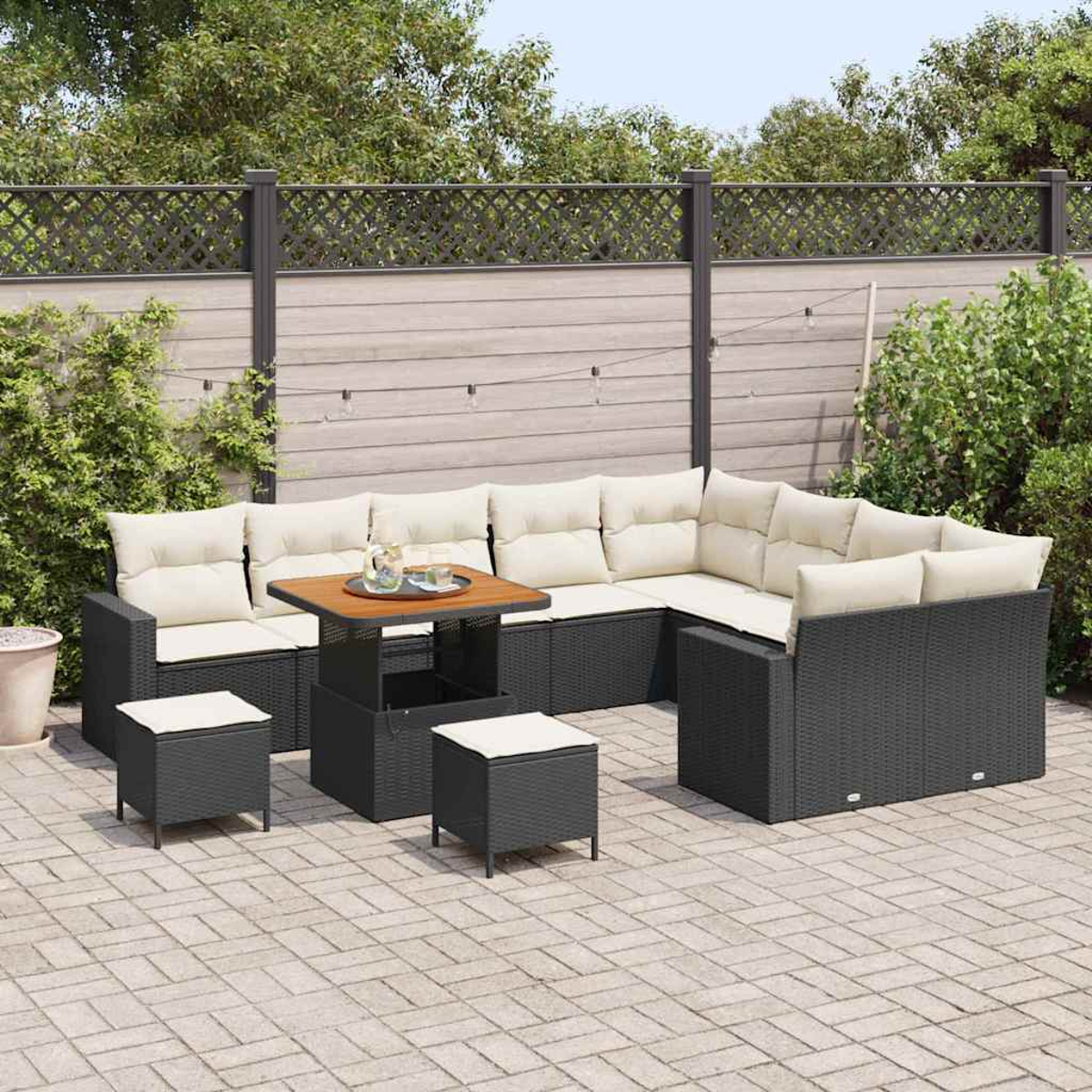 Outdoor-Terrassenset mit Ecksofa, zwei Hockern und einem Tisch. Beige Kissen auf dunkelgrauen Korbmöbeln. Hintergrund ist ein Zaun und Bäume.
