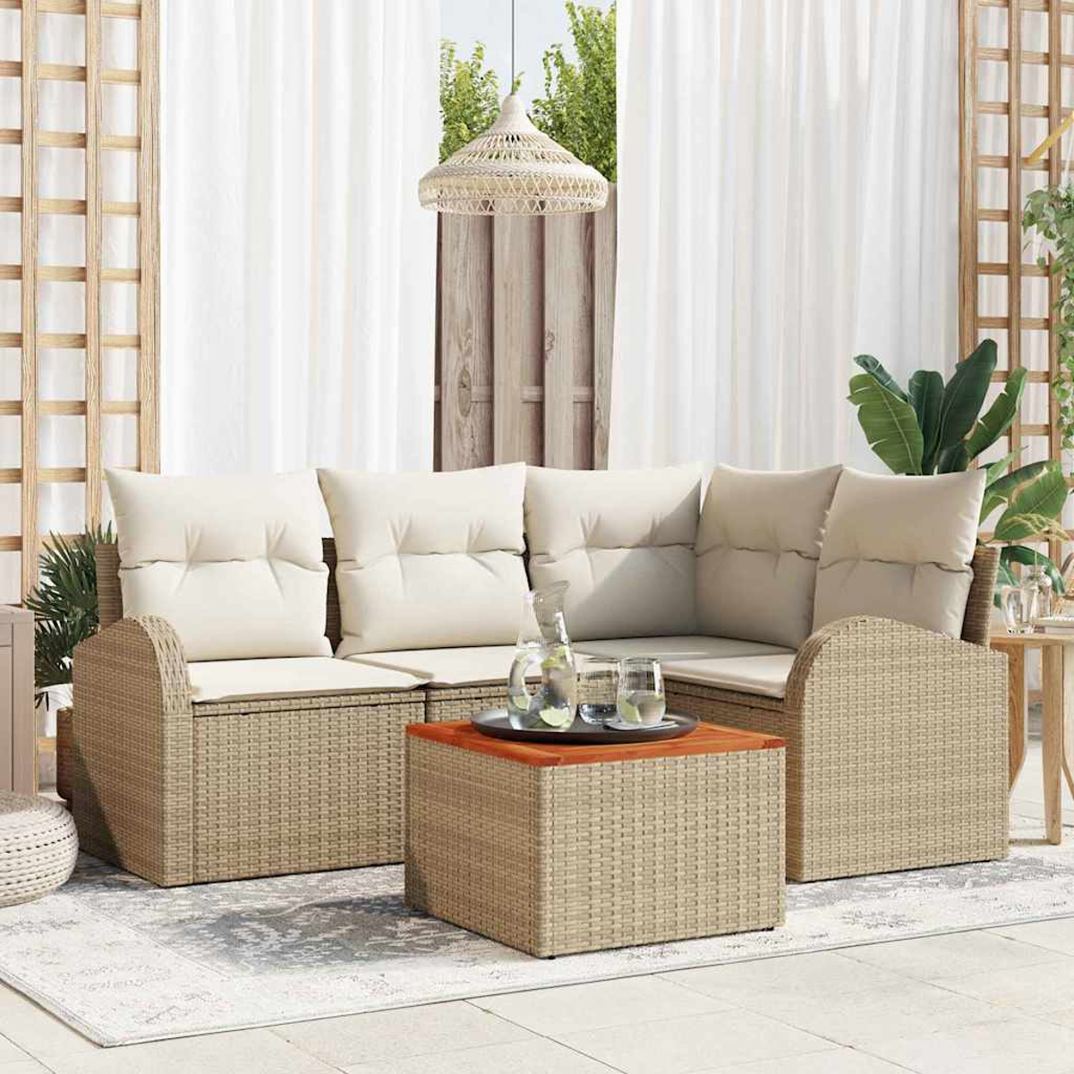 Szene im Freien mit beigem Korbsessel, Couchtisch und weißen Kissen. Klare Gläser und Kanne auf einem Tablett. Weiße Vorhänge im Hintergrund.