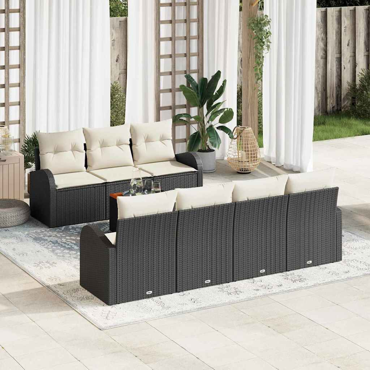 Garten-Sitzgruppe auf einer Terrasse. Enthält dunkelgraue Korbsessel mit cremefarbenen Kissen, einen Teppich, Vorhänge, Pflanzen und eine dekorative Laterne.
