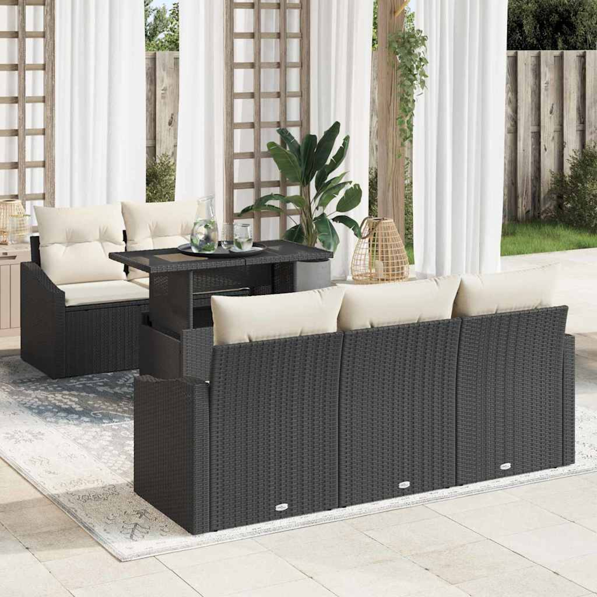 Gartenmöbel-Set mit dunklem Korbsessel, Tisch und Stuhl. Beige Kissen und durchsichtige weiße Vorhänge sind sichtbar.