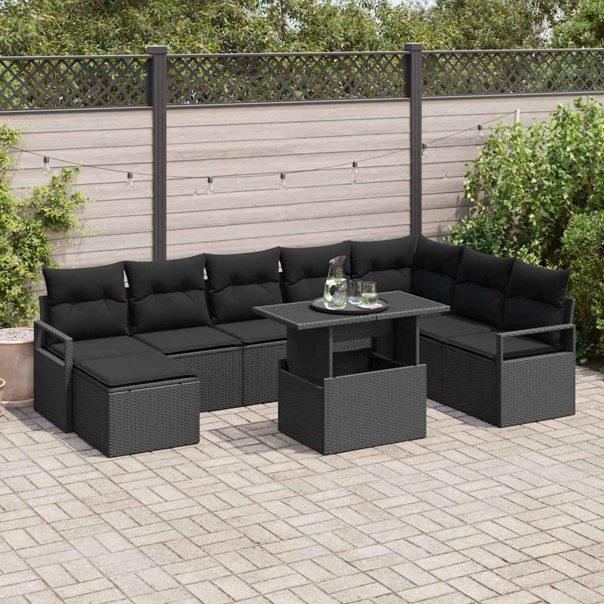 Outdoor-Ecksofa mit schwarzen Kissen und einem Tisch. Eine Wasserkaraffe und Gläser stehen auf dem Tisch. Die Szene spielt in einem Garten.