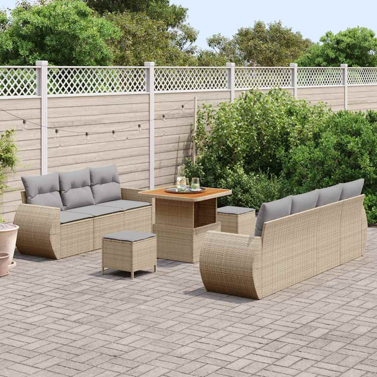 Gartenmöbel-Set aus Korbgeflecht auf einer Ziegelterrasse. Beinhaltet ein Sofa, zwei Stühle, einen Tisch und zwei Ottomanen. Grünes Laub im Hintergrund.