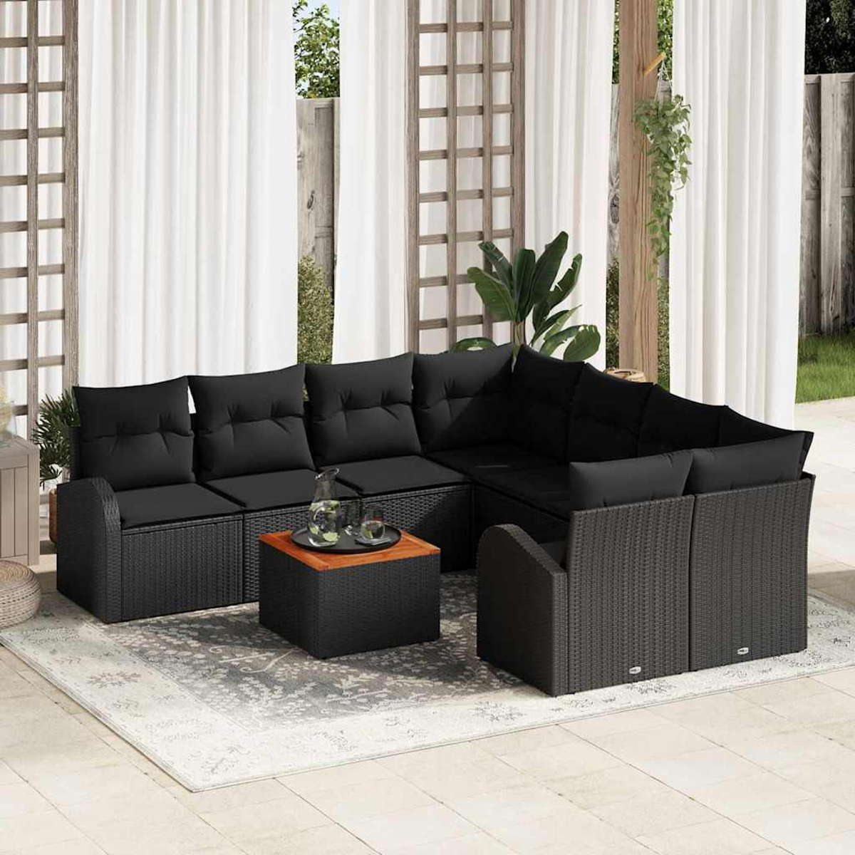 Schwarzes Outdoor-Rattansofa mit schwarzen Kissen, einem Couchtisch und einem Teppich. Weiße Vorhänge und ein Garten im Hintergrund.