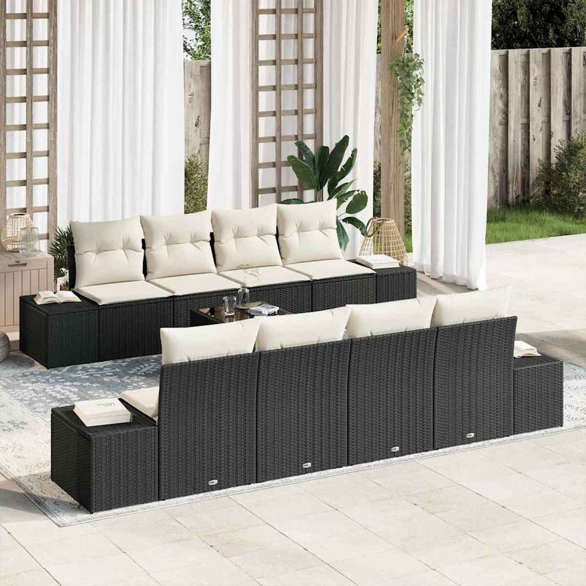 Outdoor-Sitzgruppe. Schwarze Korbsessel mit beigefarbenen Kissen. Weiße Vorhänge, Spalier und grüne Pflanzen bilden eine Gartenkulisse.
