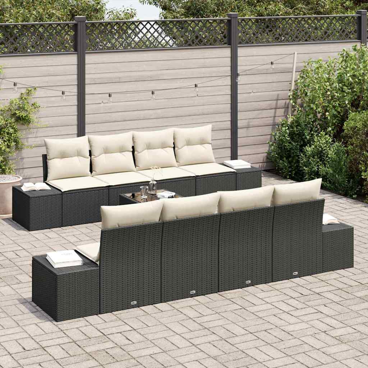 Garten-Terrassenset mit schwarzem Korbgeweberahmen, beigen Kissen und Glastisch. Auf einer Backstein-Terrasse mit Holzzaun und Grün.