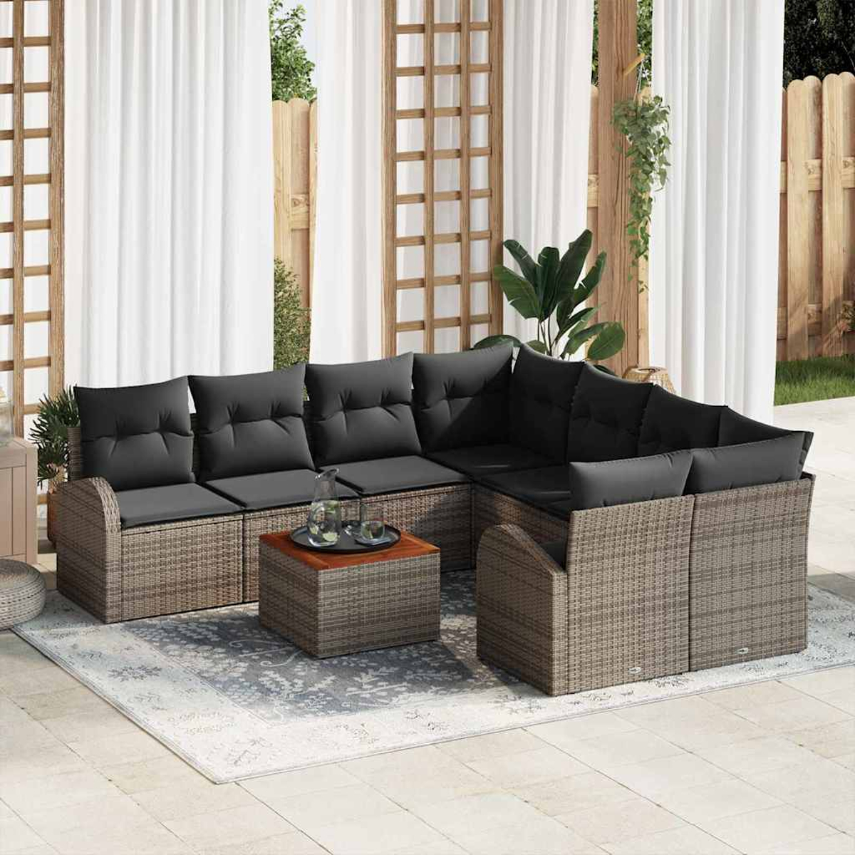 Outdoor-Ecksofa mit schwarzen Kissen, auf einem gemusterten Teppich, Couchtisch und weißen Vorhängen.