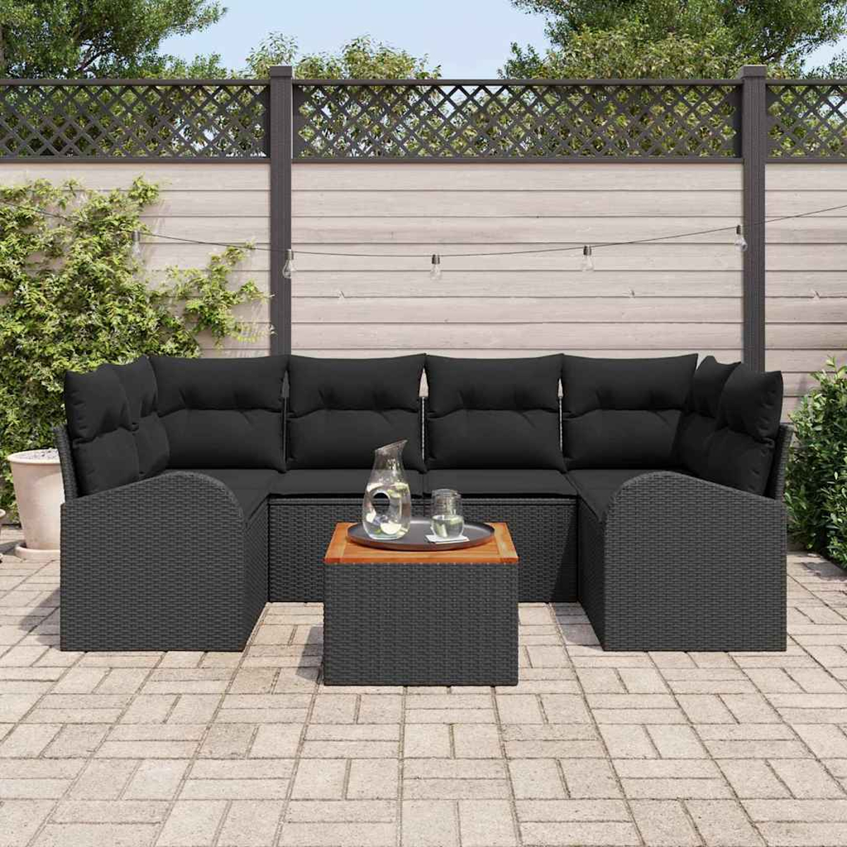 Terrassenmöbel-Set im Freien mit schwarzen Kissen und einem kleinen Tisch. Auf einer Ziegelterrasse. Hintergrund ist ein Zaun und Grün.