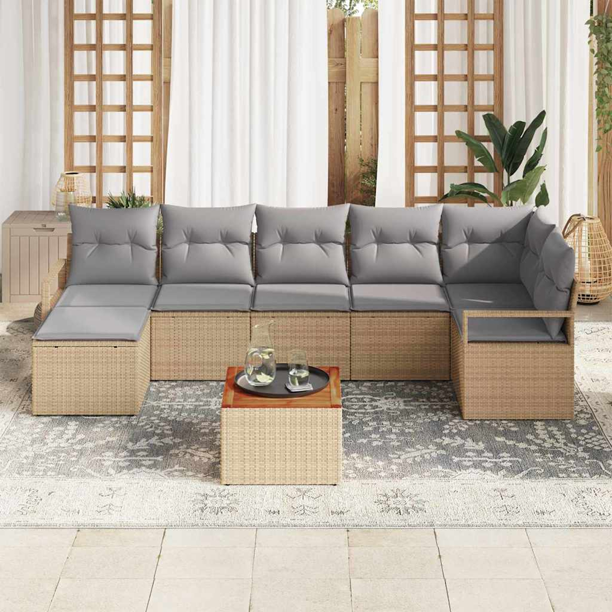 Geflochtenes Ecksofa mit grauen Kissen auf einem gemusterten Teppich, kleiner Tisch mit Getränken. Hintergrund: weiße Vorhänge und Holzgitter.
