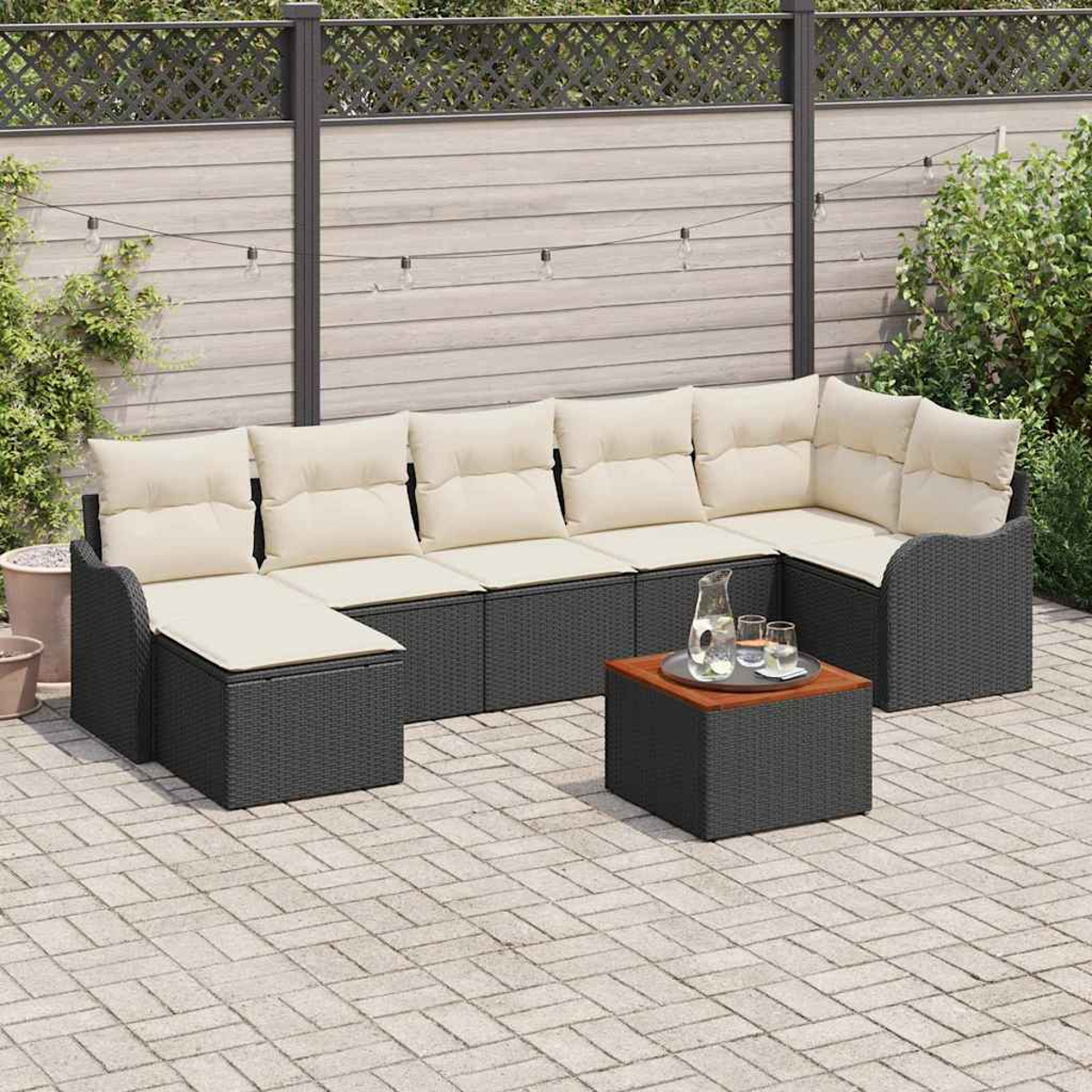 Outdoor-Ecksofa mit cremefarbenen Kissen. Davor steht ein kleiner Tisch mit Wasser und Gläsern. Im Hintergrund ein Zaun und Pflanzen.
