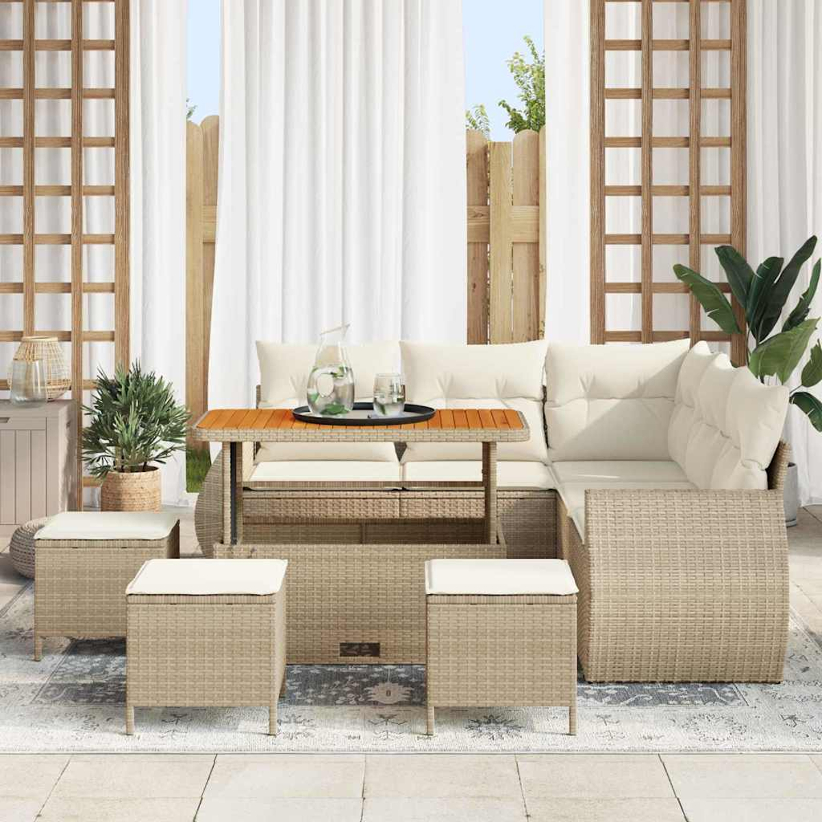 Gartenmöbel-Set aus Korbgeflecht mit Tisch, Sofa und Hockern. Weiße Kissen, Wassergläser und Pflanzen auf einem Teppich.