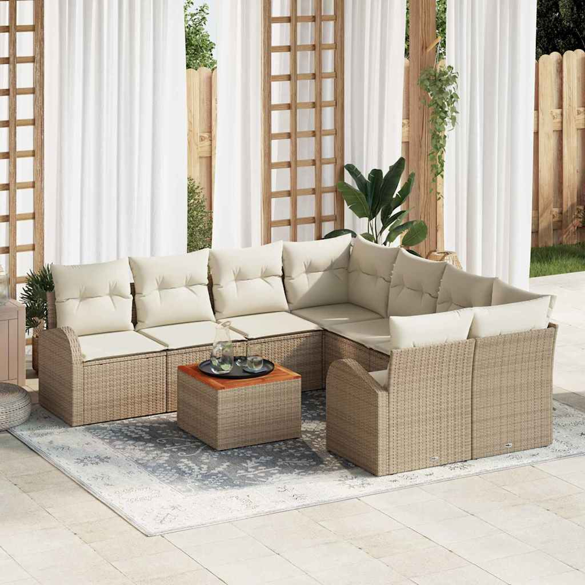 Outdoor-Sofa aus Korbgeflecht mit beigen Kissen und einem kleinen Holztisch. Weiße Vorhänge und ein Holzzaun im Hintergrund.