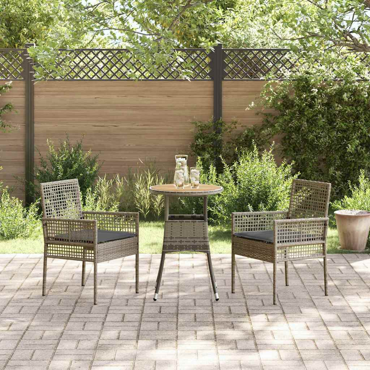 Szene auf der Terrasse mit zwei Stühlen und einem Tisch. Ein Holzzaun im Hintergrund mit grünen Büschen und einem Topf. Die Stühle haben Kissen.