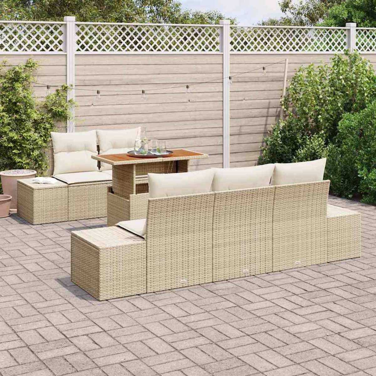 Gartenmöbel-Set. Korbsessel, Tisch und Sitzgelegenheiten. Beige Kissen. Gepflasterter Boden. Holzzaun im Hintergrund.