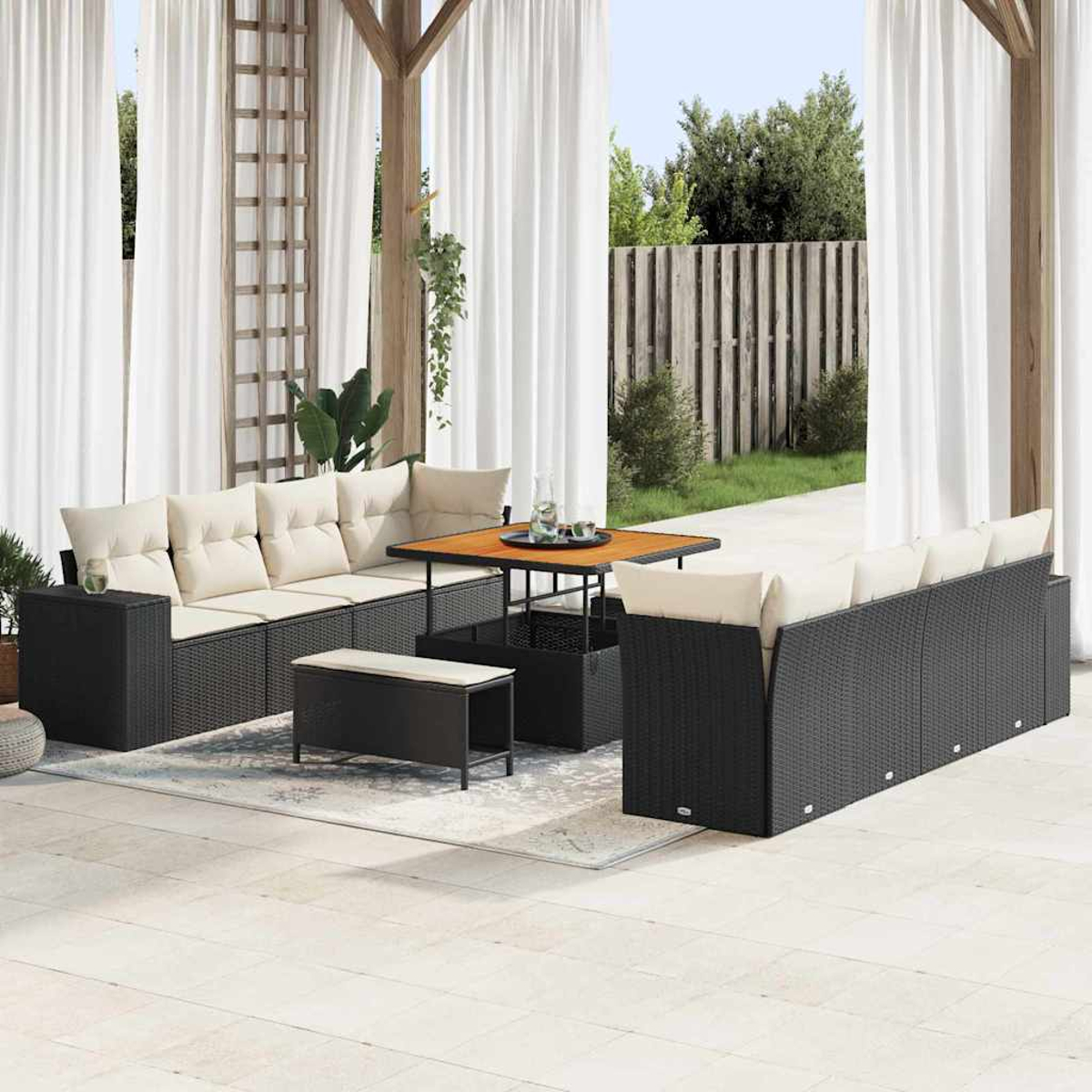 Terrassengarnitur mit schwarzen Korbsesseln, cremefarbenen Kissen und Holztisch. Weiße Vorhänge und eine Holzpergola rahmen die Szene ein.