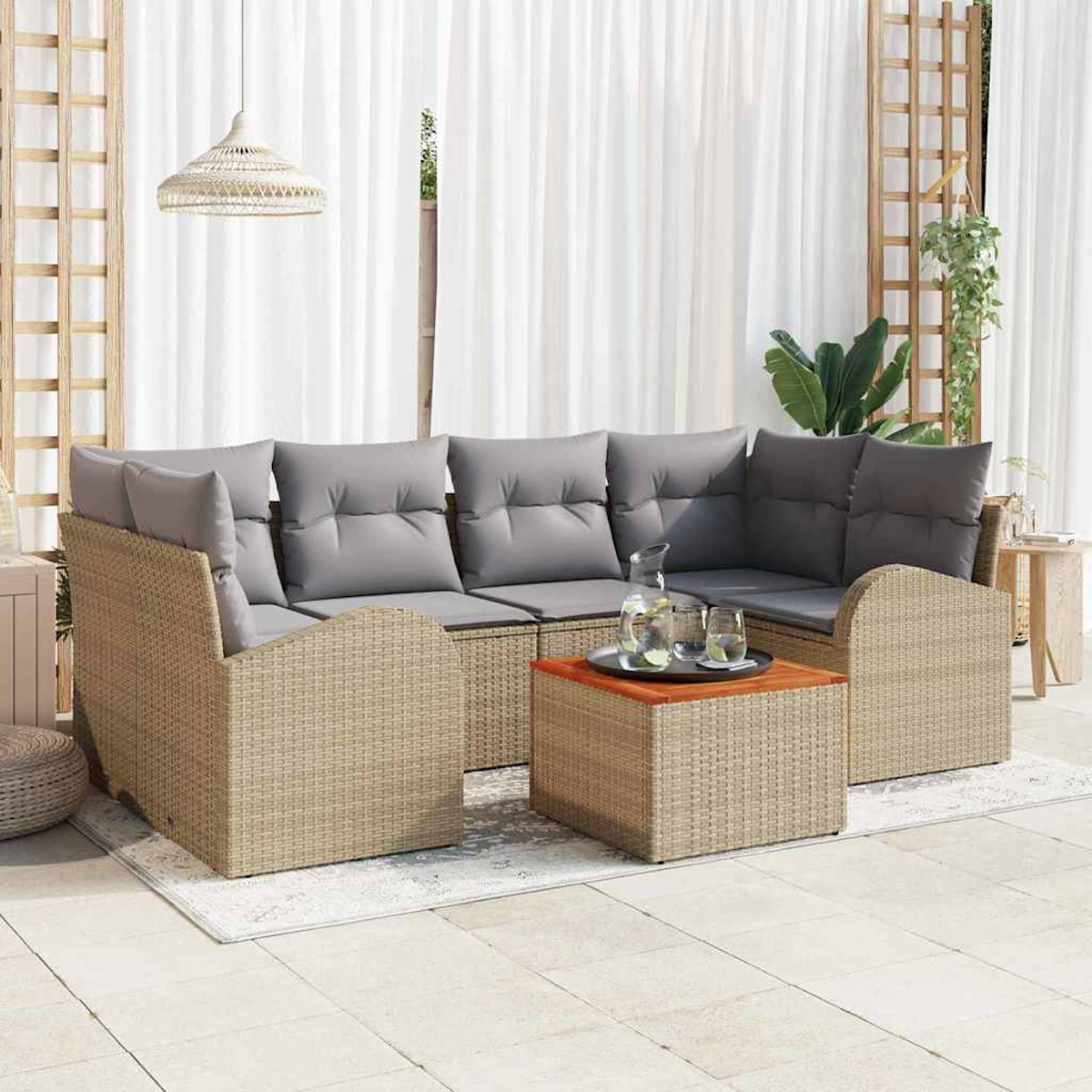 Outdoor-Korbsofa mit grauen Kissen, Holztisch mit Getränken und weißen Vorhängen im Hintergrund.