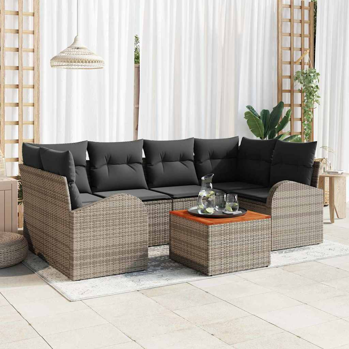 Outdoor-Ecksofa mit grauen Kissen. Ein Holztisch mit Gläsern und einem Krug. Weiße Vorhänge im Hintergrund.
