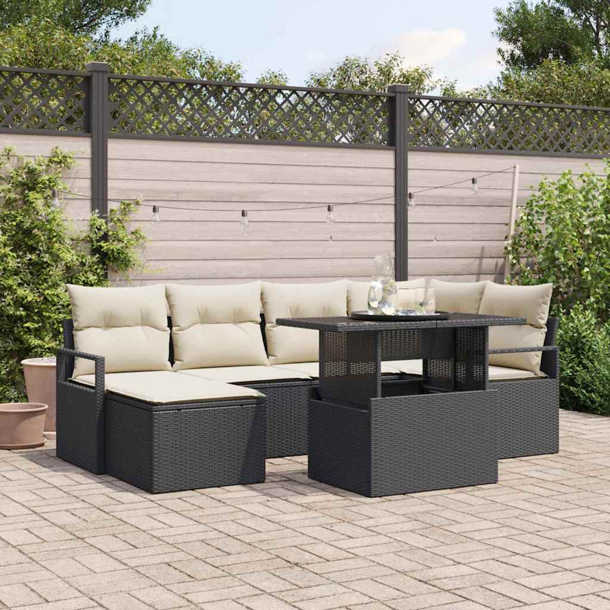 Garten-Terrassenset mit grauen Korbmöbeln, beigefarbenen Kissen und einem Tisch mit Hubplatte. Der Hintergrund umfasst einen Zaun und Grün.