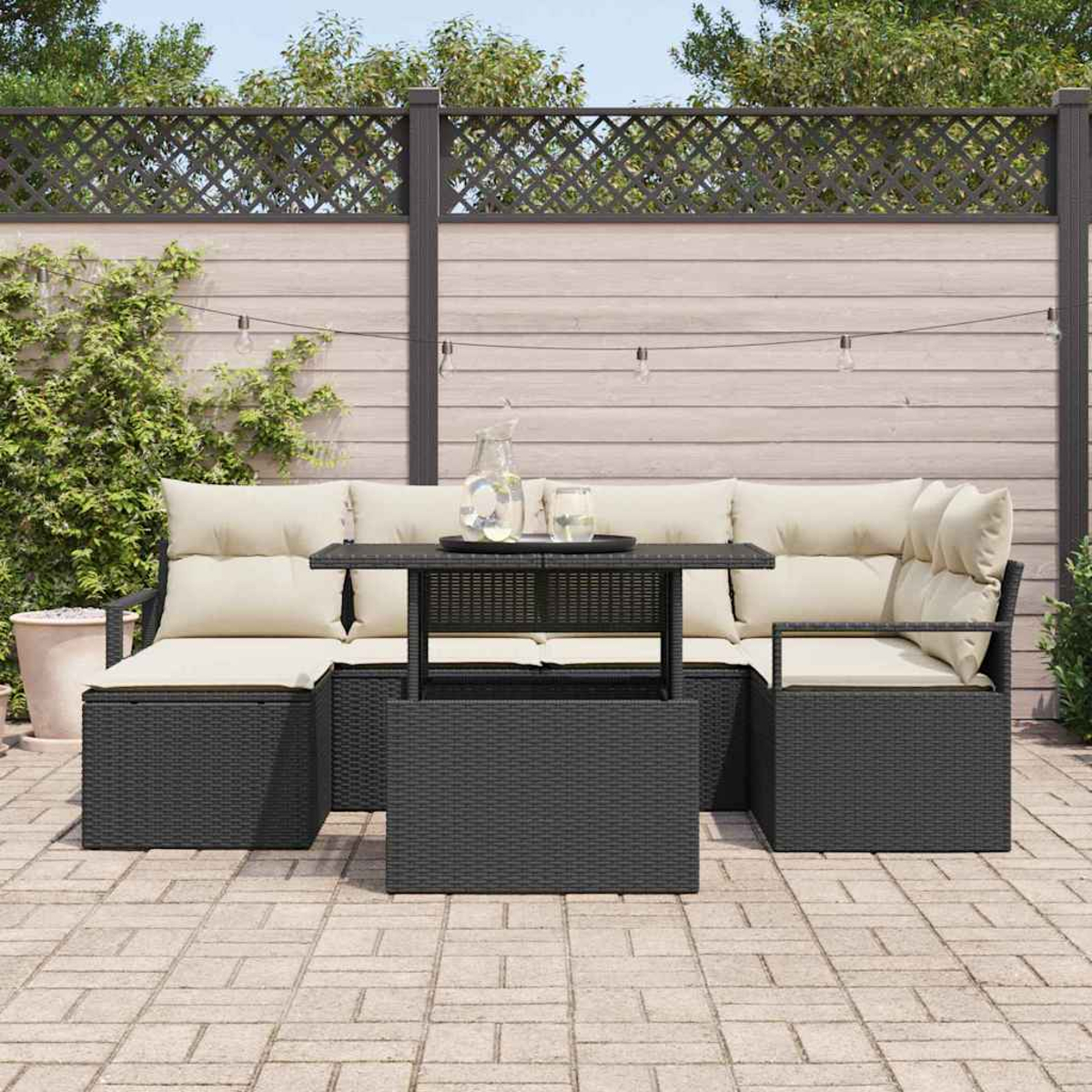 Terrassenset mit schwarzem Korbmöbel, beigen Kissen und einem Couchtisch. Ein Zaun und Pflanzen sind im Hintergrund.