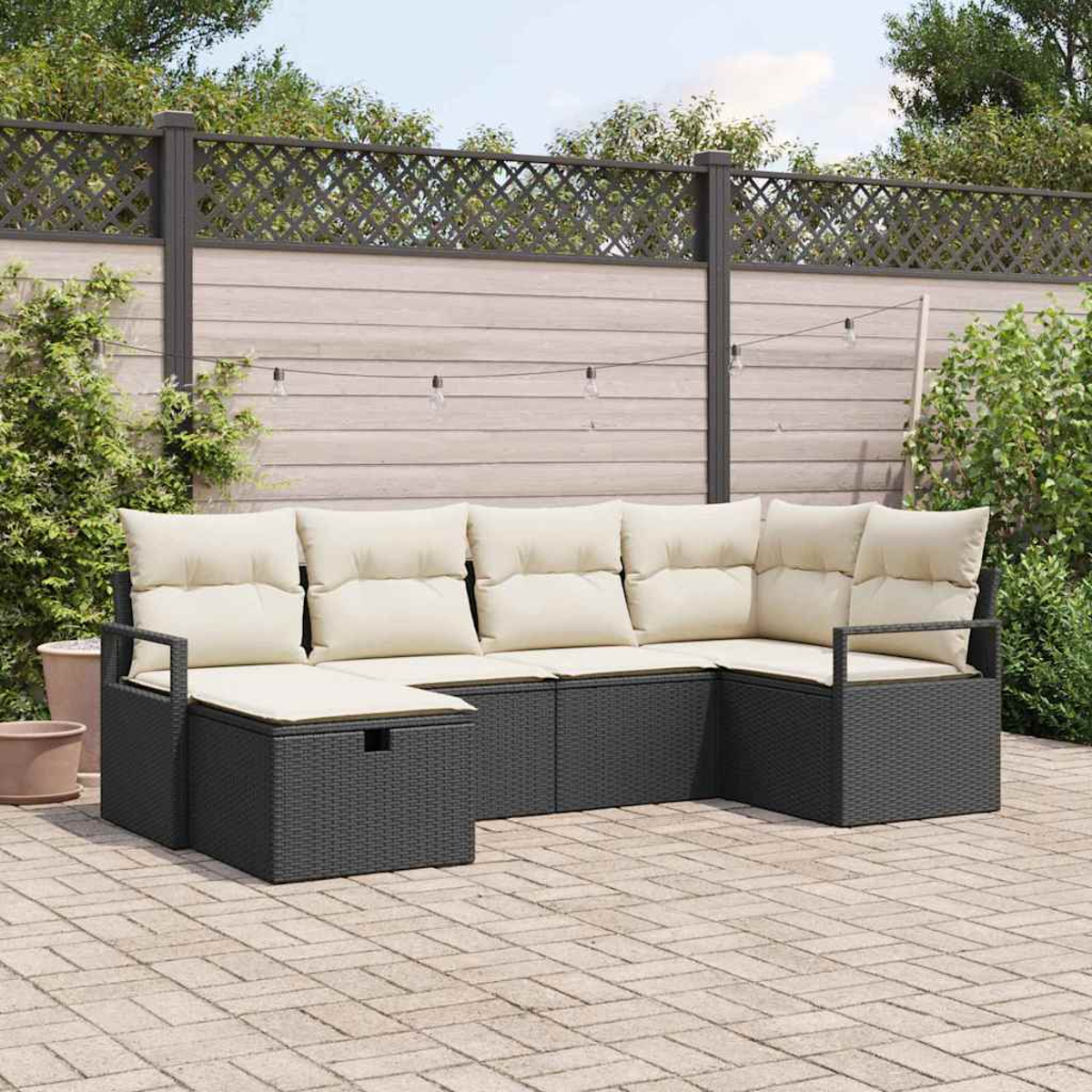 Dunkelgraues Outdoor-Ecksofa mit cremefarbenen Kissen auf einer Ziegelterrasse, mit Holzzaun und Pflanzen im Hintergrund.