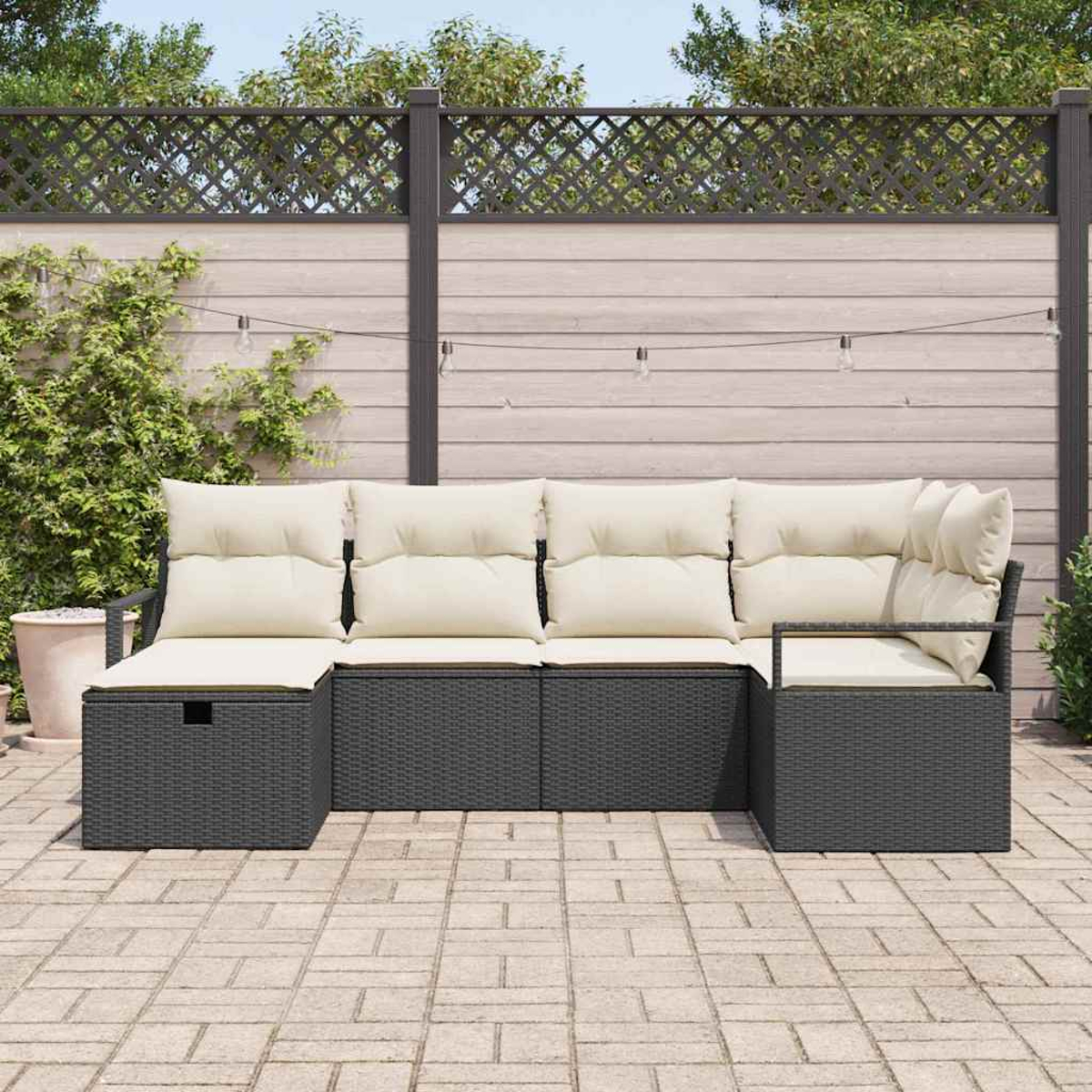 Outdoor-Ecksofa mit cremefarbenen Kissen auf einer Terrasse. Das Sofa ist dunkelgrau, mit Holzzaun und Lichterketten im Hintergrund.