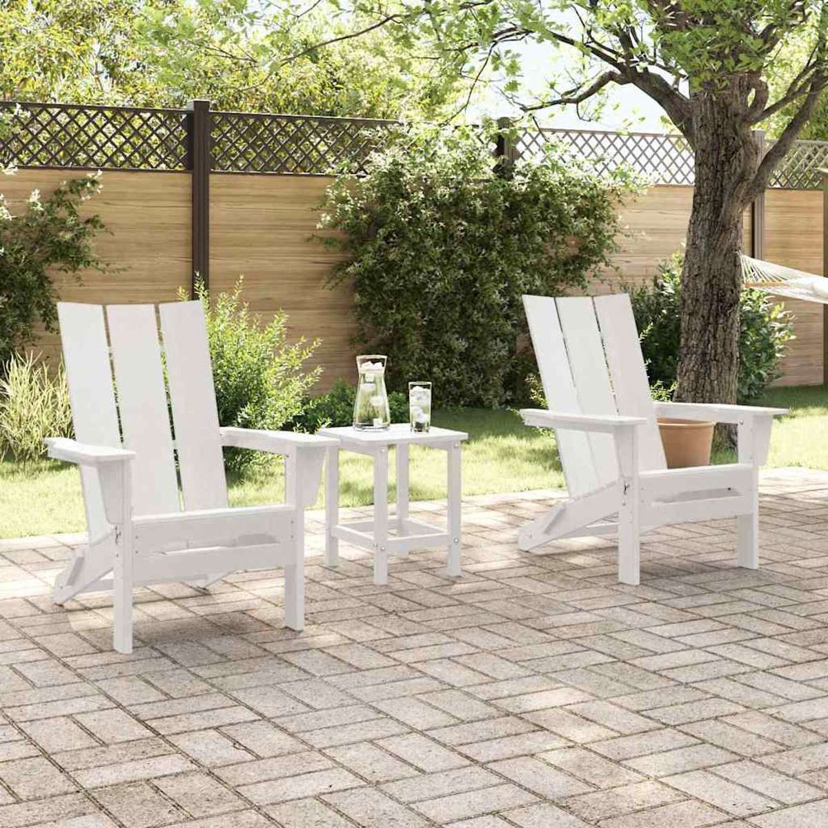 Zwei weiße Adirondack-Stühle und ein kleiner Tisch auf einer Ziegelterrasse. Eine Kanne und Gläser stehen auf dem Tisch. Grünes Laub und Bäume im Hintergrund.