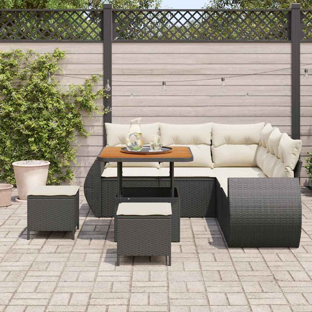 Terrassenset mit Ecksofa, Hockern und Tisch mit Getränken. Im Hintergrund ein Zaun und Kletterpflanzen.