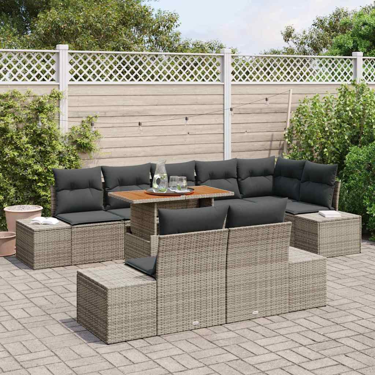 Garten-Sitzgruppe mit grauen Kissen und einem Holztisch auf einer gepflasterten Terrasse. Ein weißer Gitterzaun und Grün im Hintergrund.