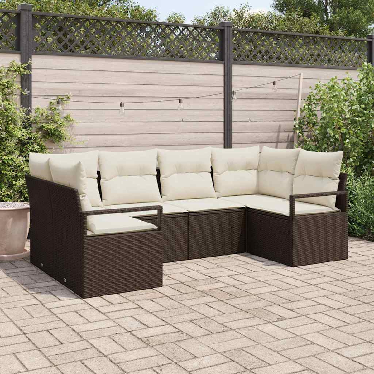 Ein braunes Rattan-Ecksofa mit cremefarbenen Kissen steht auf einer Ziegelterrasse. Ein Holzzaun und Grünzeug sind im Hintergrund.