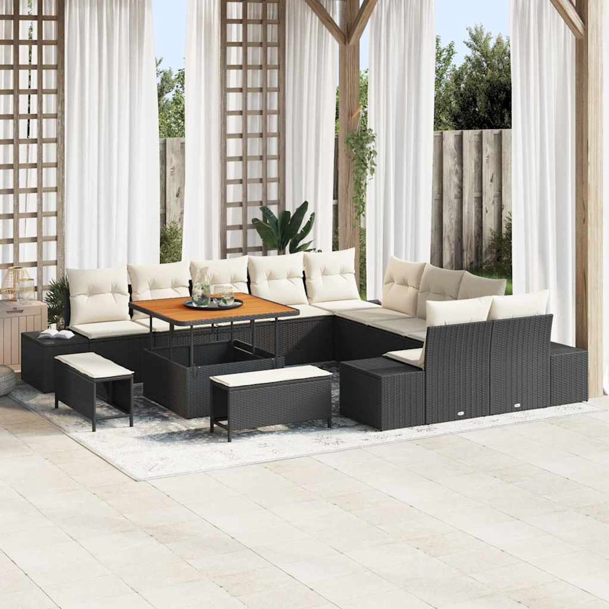 Outdoor-Terrassenset: schwarze Korbmöbel mit cremefarbenen Kissen, Holztisch, weiße Vorhänge und ein Teppich auf einer Terrasse.