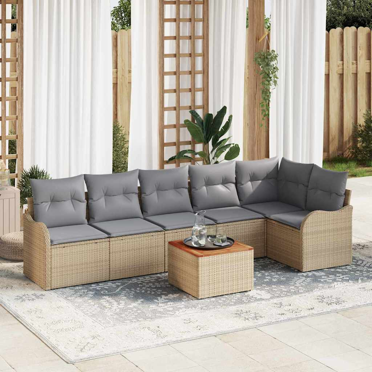Ein Ecksofa im Freien mit grauen Kissen steht auf einem gemusterten Teppich. Ein quadratischer Tisch trägt ein Tablett mit Krug und Gläsern.