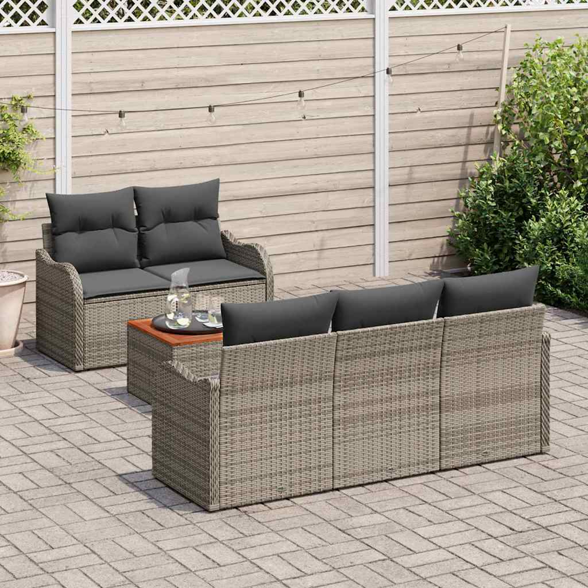 Terrassenset im Freien mit grauen Kissen. Enthält zwei Sofas, einen Couchtisch und eine Backsteinterrasse. Holzzaun und Grün im Hintergrund.