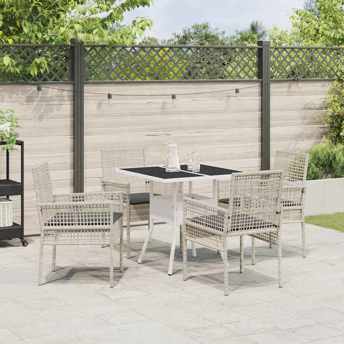 Terrassenset im Freien: ein weißer Tisch mit schwarzer Platte, vier beigefarbene Stühle mit Kissen, ein Zaun und ein paar Gläser.